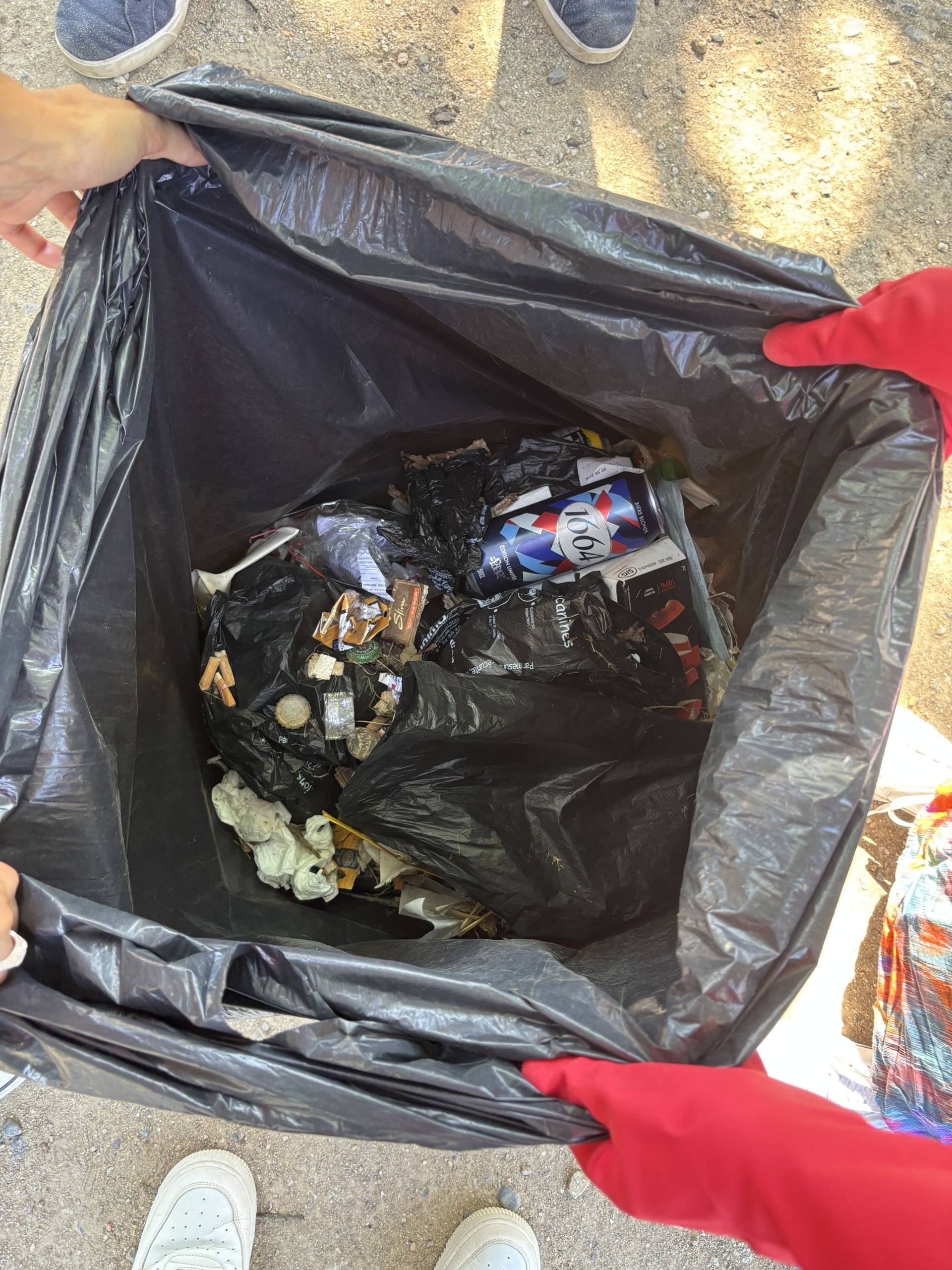 Photo du contenu du sac poubelle rempli par l'équipe de ramassage de Decasoft montrant différents types de déchets (mégots, capsules, cannettes, verre, sacs plastique, papiers en tout genre, etc...)